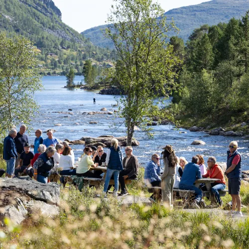 Folk koser seg på benker langs Otra ved Hovdestøylen