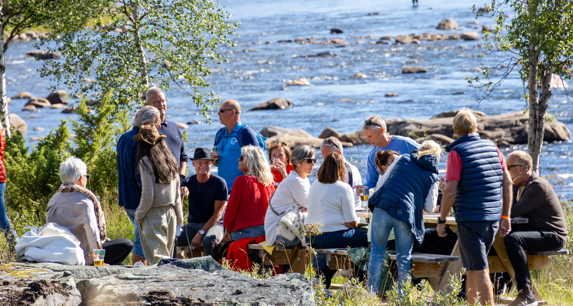 Folk koser seg på benker langs Otra ved Hovdestøylen