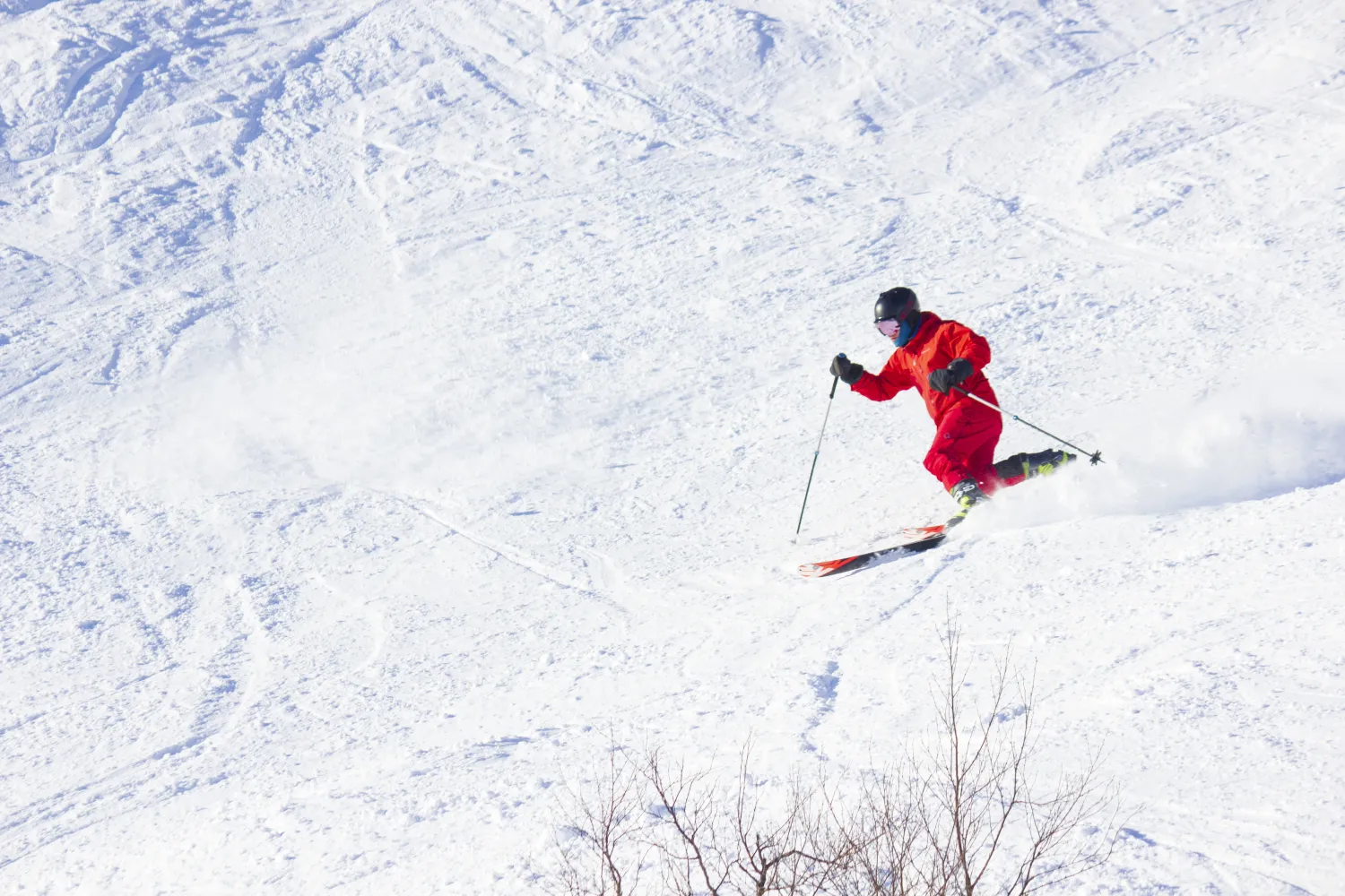 Telemarkkjører i rød skidress som svinger ned en snødekt bakke.