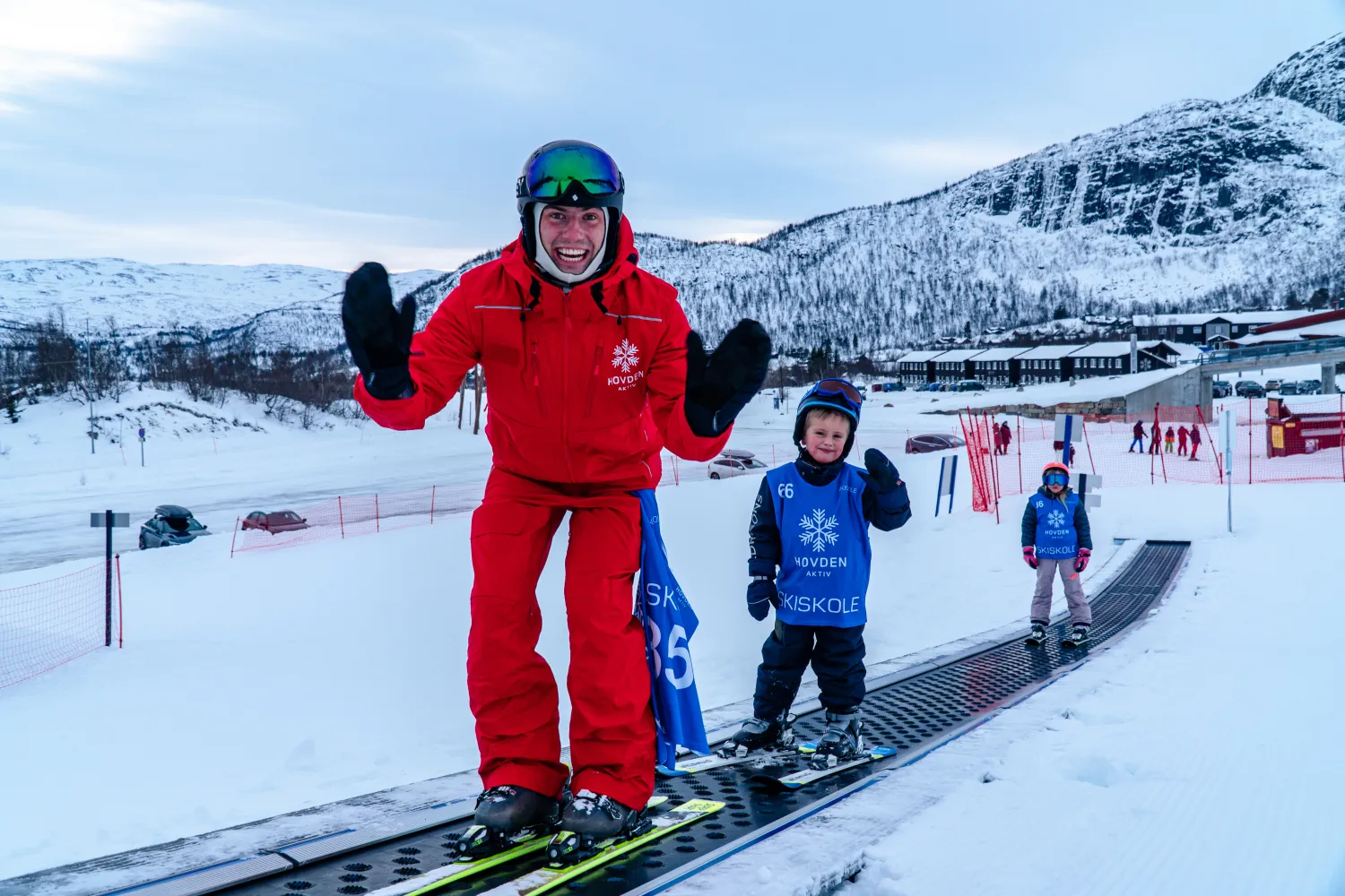 Skiinstruktør i rød skidress sammen med to barn på ski i et skibånd hos Hovden Aktiv.