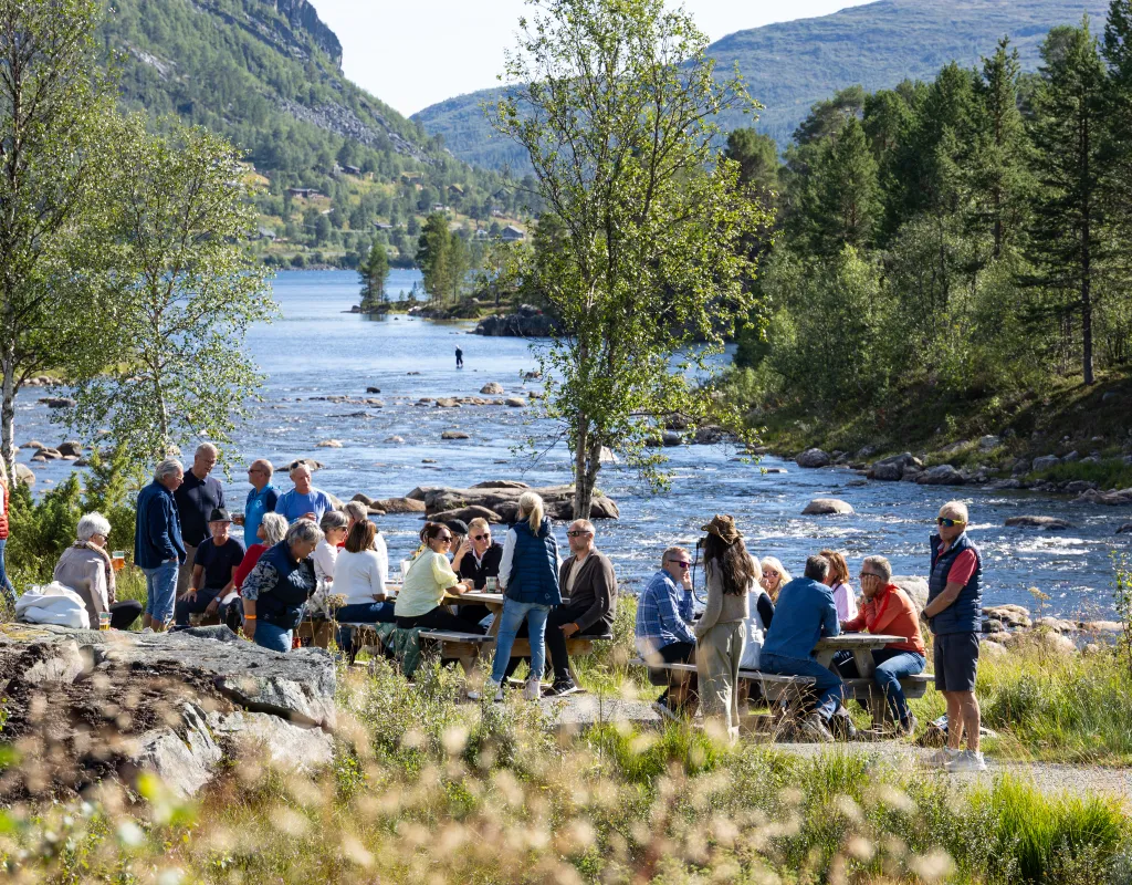 Folk koser seg på benker langs Otra ved Hovdestøylen