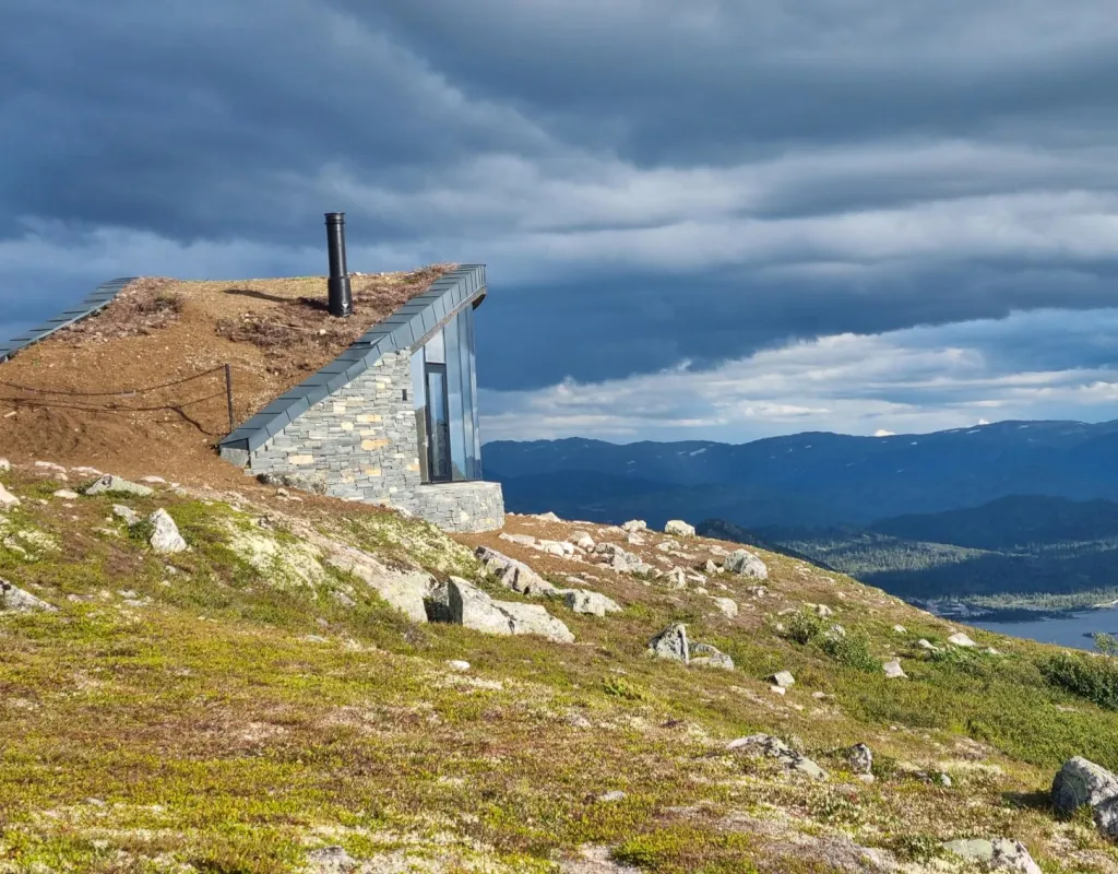 Dagsturhytte i stein med utsikt over fjell og innsjø