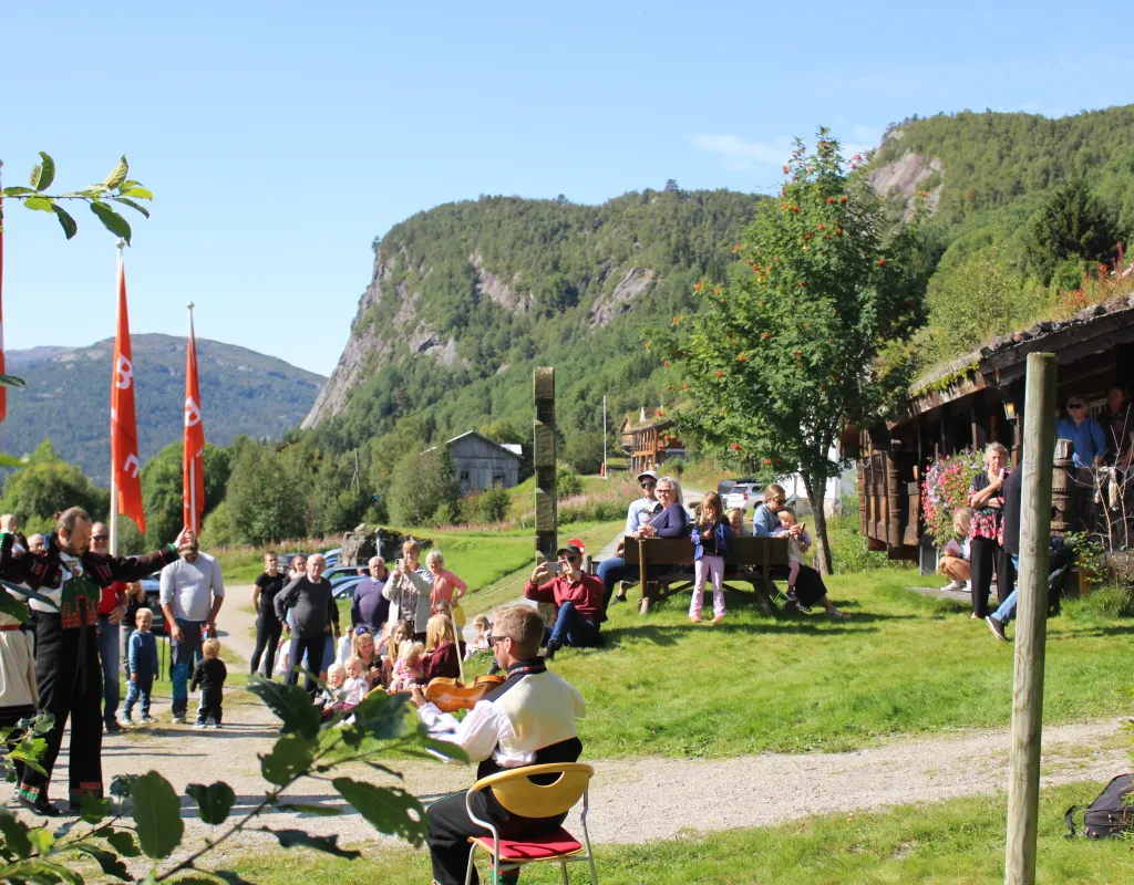 Folk koser seg på bygdetunet Lislestog, bunadskledde folk danser og spiller fele
