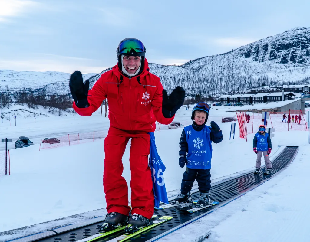 Skiinstruktør i rød skidress sammen med to barn på ski i et skibånd hos Hovden Aktiv.